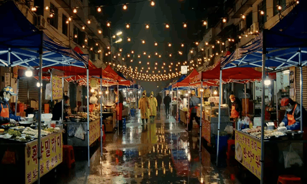 AI generated video: A night market in the rain, three shots in one clip. First a wide of the lane…
