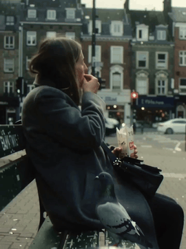 AI generated video: A realistic candid handheld video in a city square. A woman sits on a bench…